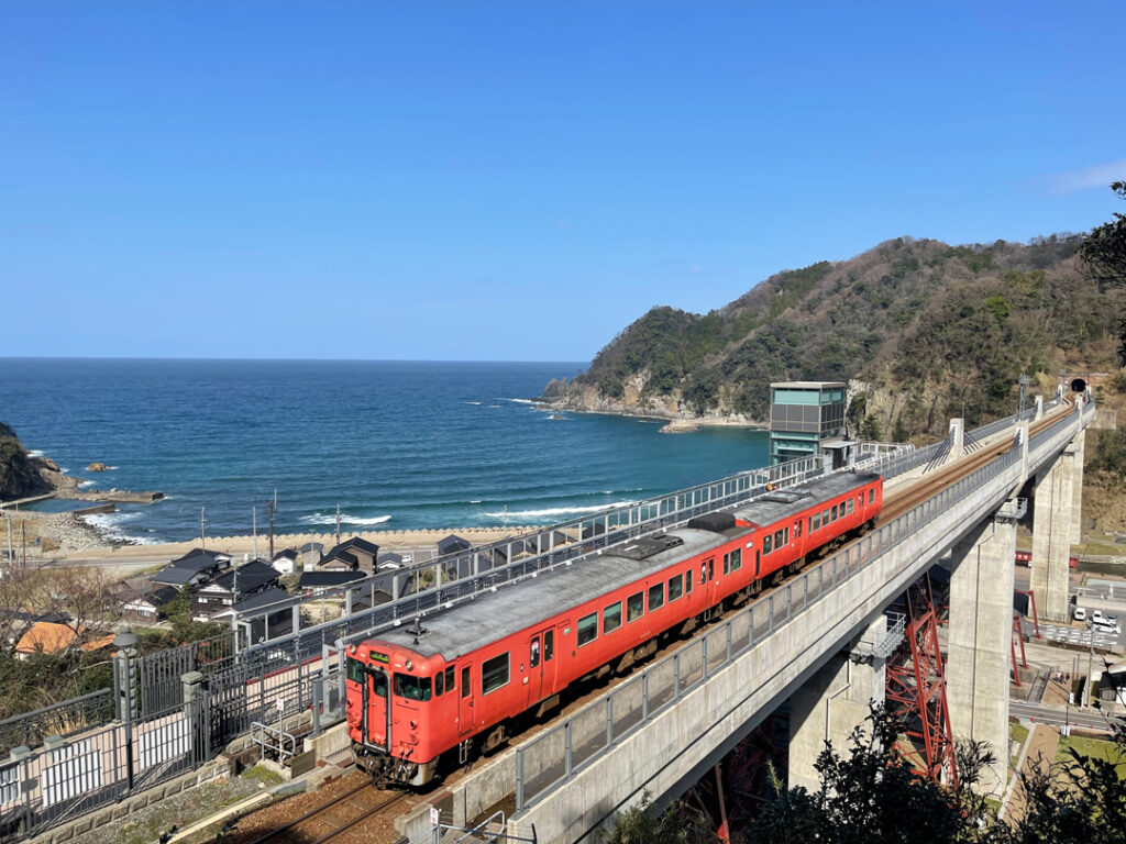 日本海をバックに橋梁を渡るR山陰本線の列車
